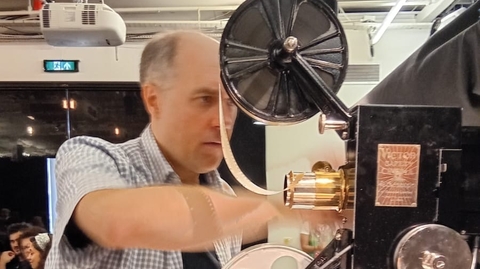 A still of Christopher Bird operating a projector.