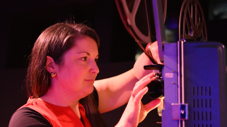 A still of Rosie Taylor operating a projector.