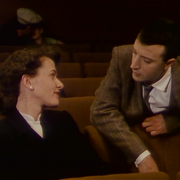 A photo of a man leaning over a cinema seat to talk to a woman.