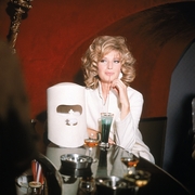 Woman with curly blonde hair in a white outfit seated at a bar table with multiple drinks.