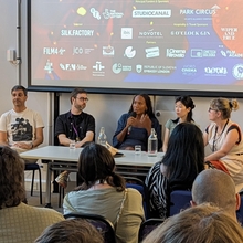 A panel of people sitting in front of an audience with a screen behind them.