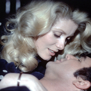 A close-up of a man and a woman embracing and leaning in for a kiss in a dimly lit setting.