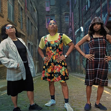 Three people standing outside looking at the camera with their hands on their hips.