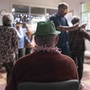 Elderly person wearing a green party hat watches a lively holiday gathering with dancing and festive decorations in a cozy room.