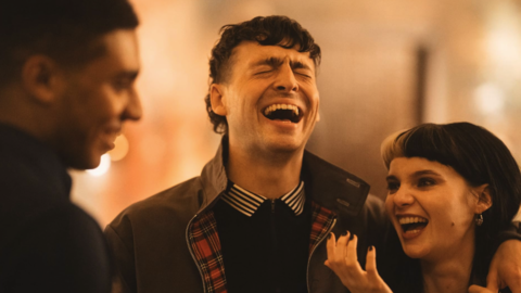Three people engaged in conversation in a warmly lit indoor setting at night.