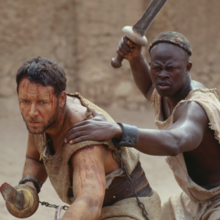 Two men in tattered garments, one holding a chained dagger, the other raising a sword in a desert-like setting.