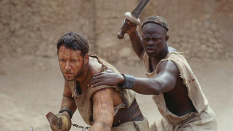Two men in tattered garments, one holding a chained dagger, the other raising a sword in a desert-like setting.