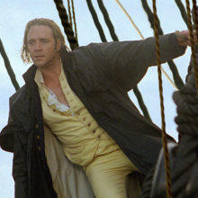 Person in vintage sailor outfit with yellow pants and ruffled shirt stands on ship deck, holding onto ropes.