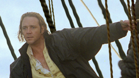 Person in vintage sailor outfit with yellow pants and ruffled shirt stands on ship deck, holding onto ropes.