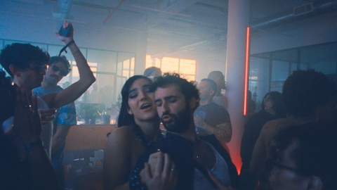 A dimly lit indoor party with people dancing and socialising amidst fog and coloured lights.