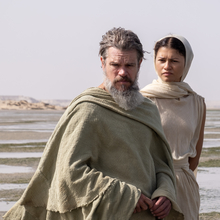 A man and a woman standing next to each other outside draped in floaty clothes.