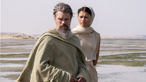 A man and a woman standing next to each other outside draped in floaty clothes.