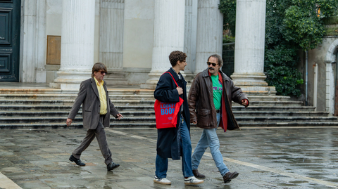 Three people walk on wet stone pavement near large white columns outside a classical-style building.