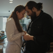 A couple holding hands and facing each other inside a softly lit living room.