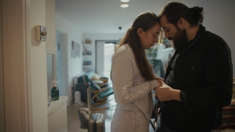 A couple holding hands and facing each other inside a softly lit living room.