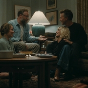 Four people sitting and talking in a cozy living room around a wooden coffee table with drinks and snacks.