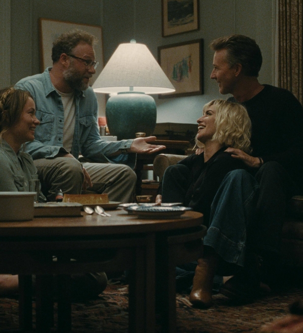 Four people sitting and talking in a cozy living room around a wooden coffee table with drinks and snacks.