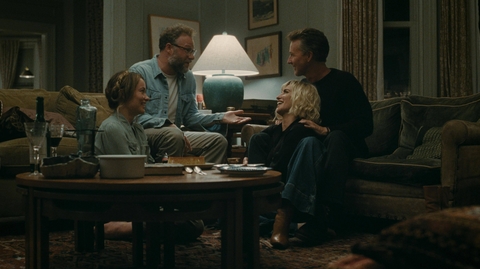 Four people sitting and talking in a cozy living room around a wooden coffee table with drinks and snacks.
