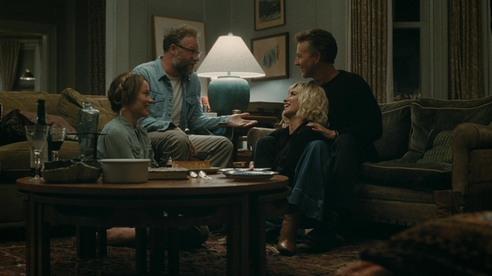Four people sitting and talking in a cozy living room around a wooden coffee table with drinks and snacks.