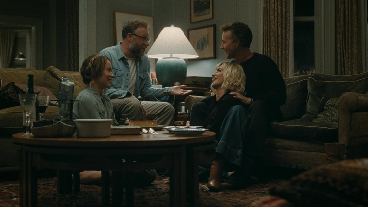 Four people sitting and talking in a cozy living room around a wooden coffee table with drinks and snacks.