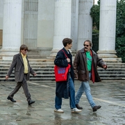 Three men walk across a square in the rain