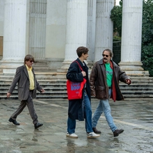 Three men walk across a square in the rain