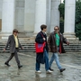 Three men walk across a square in the rain