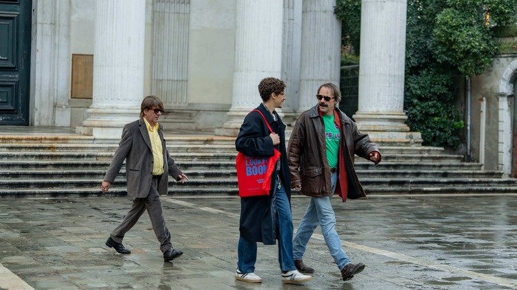 Three men walk across a square in the rain