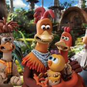 Animated chickens with expressive faces gathered outdoors in a colourful, lush village setting.
