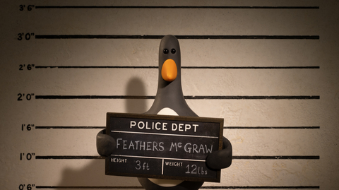 Penguin holding a police mugshot board in front of a height chart, named Feathers McGraw, 3 ft tall and weighing 12 lbs.