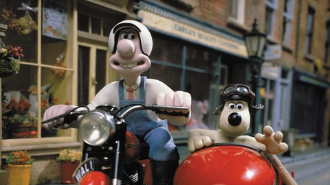Claymation characters Wallace and Gromit riding a motorcycle with a sidecar on a quiet street with brick buildings.