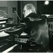 Black and white photo of a man playing multiple keyboards and synthesizers in a studio setting.