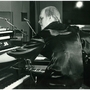 Black and white photo of a man playing multiple keyboards and synthesizers in a studio setting.