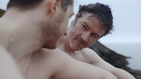 A still of two men sitting on a beach looking at each other.