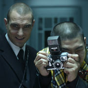 Two men standing next to each other - one taking a photo with a camera