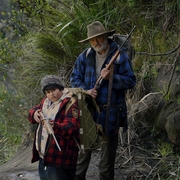 A still of a man and a child standing next to each other both holding guns.