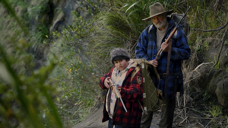 A still of a man and a child standing next to each other both holding guns.