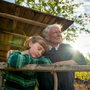 A grandmother and her granddaughter lean against a ledge on a veranda in the summer sun.