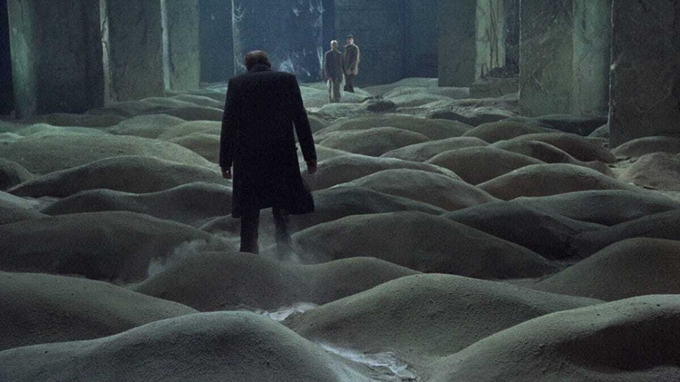 A man walks across piles of sand towards two men in the background.
