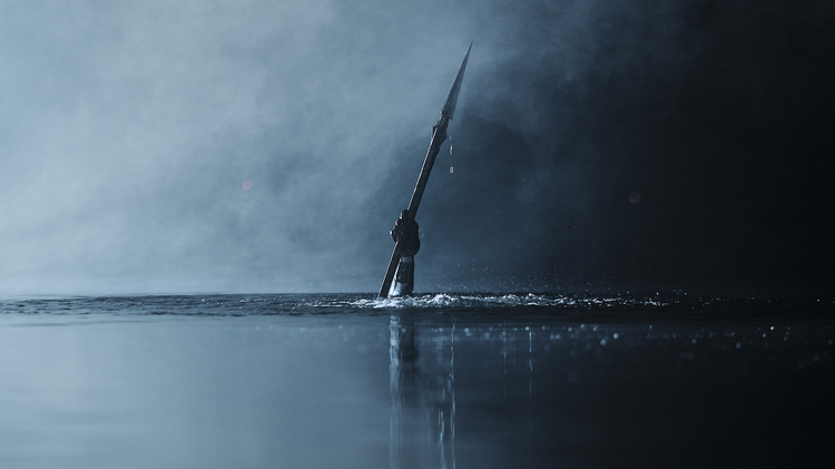 Hand holding a spear emerging from dark, misty water with droplets falling and reflections on the surface.
