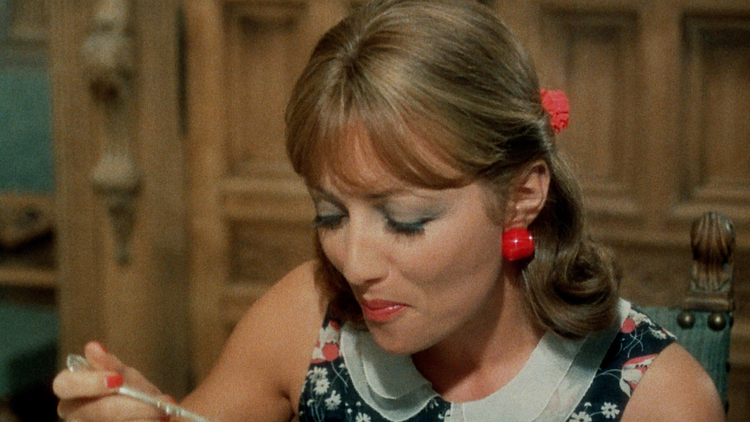 Woman in floral dress with red earrings and hair accessory eating with a spoon, seated in a vintage wooden chair.
