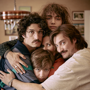 Five people closely embracing each other in a warm group hug inside a cozy room.