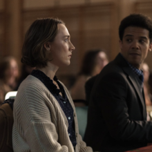 A woman stares pensively straight ahead whilst a man in a suit anticipates to hear an answer from her.