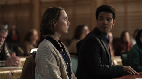 A woman stares pensively straight ahead whilst a man in a suit anticipates to hear an answer from her.