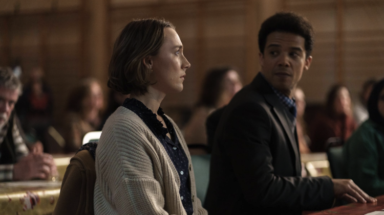 A woman stares pensively straight ahead whilst a man in a suit anticipates to hear an answer from her.
