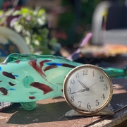 Objects from a 1960s Dominican front room including a green glass fish ornament and a small metal clock