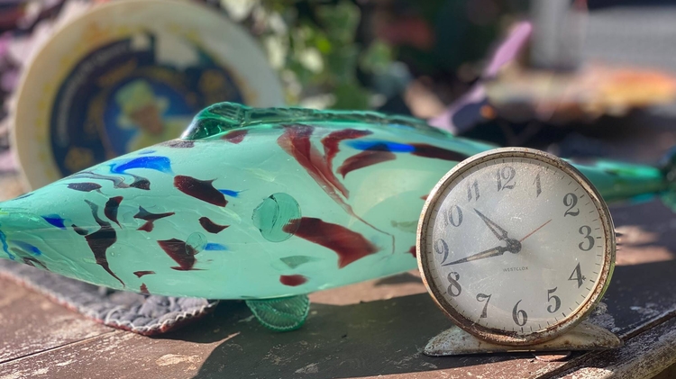 Objects from a 1960s Dominican front room including a green glass fish ornament and a small metal clock