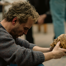 A man sits with a bowed head holding a skull in his hands