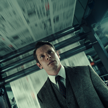 A man in a suit and tie stands underneath a large newspaper printing press