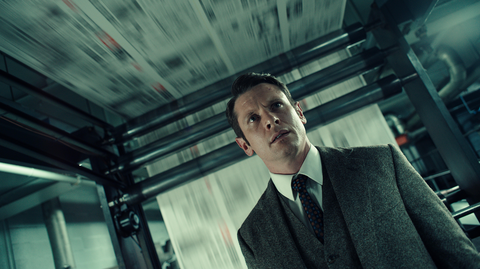 A man in a suit and tie stands underneath a large newspaper printing press
